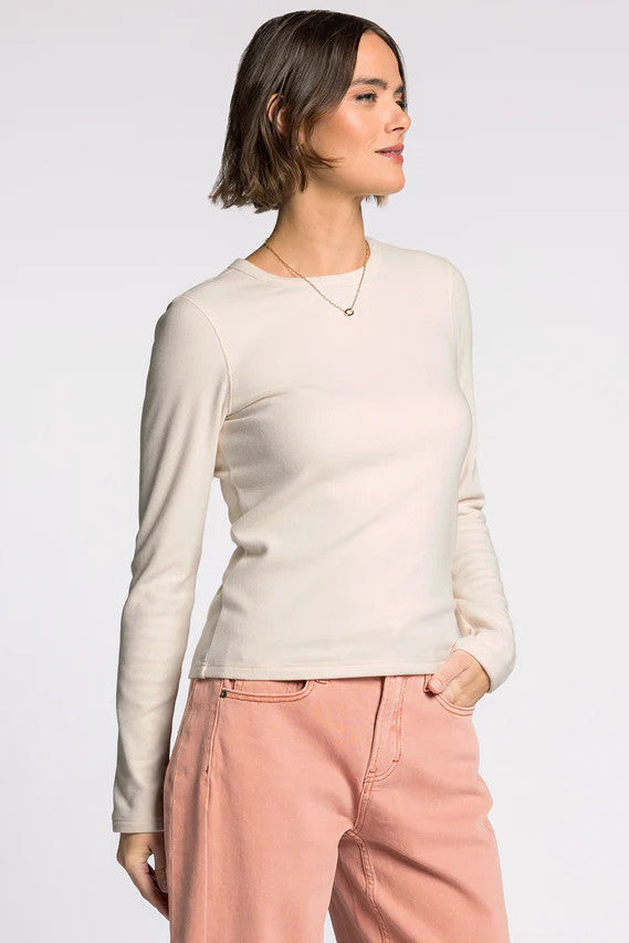 Woman wearing a white long-sleeve top and pink pants on a white background with her one hand in her pockets