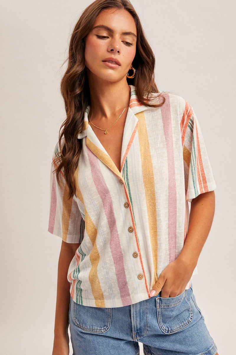 Woman wearing a colorful striped shirt and blue jeans shorts against a plain background