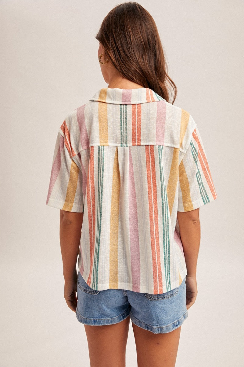 Person wearing a colorful striped shirt and denim shorts on a plain background