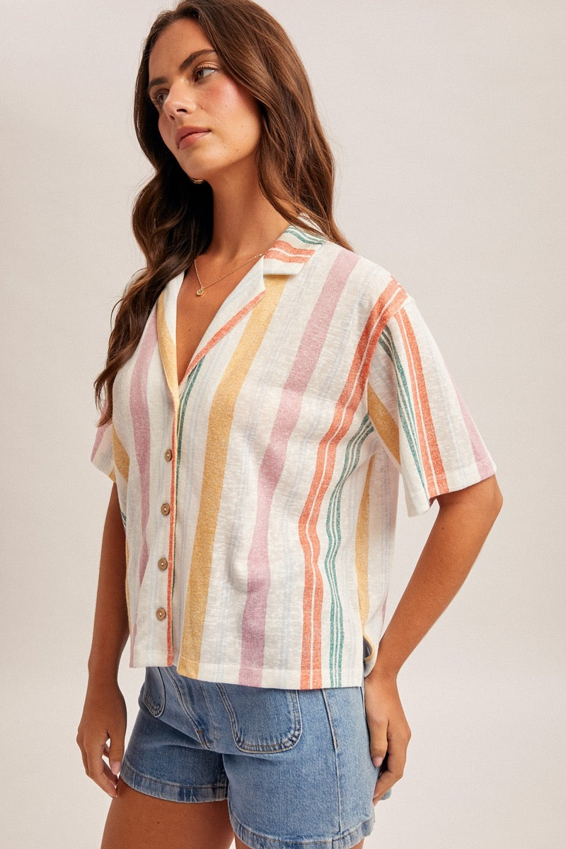 Woman wearing a colorful striped shirt and denim shorts on a plain background