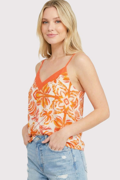 Woman wearing an orange floral tank top and blue jeans on a light gray background