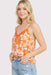Woman wearing an orange floral tank top and blue jeans on a light gray background
