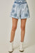 Person wearing light blue embroidered shorts with white cowboy boots on a plain background