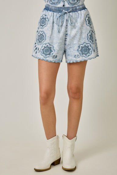 Denim shorts with floral embroidery patterns worn by a person on a plain background