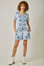 Woman wearing a blue floral patterned outfit with white boots on a plain background