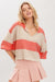 Woman wearing a coral and beige sweater with s pink skirt against a white background