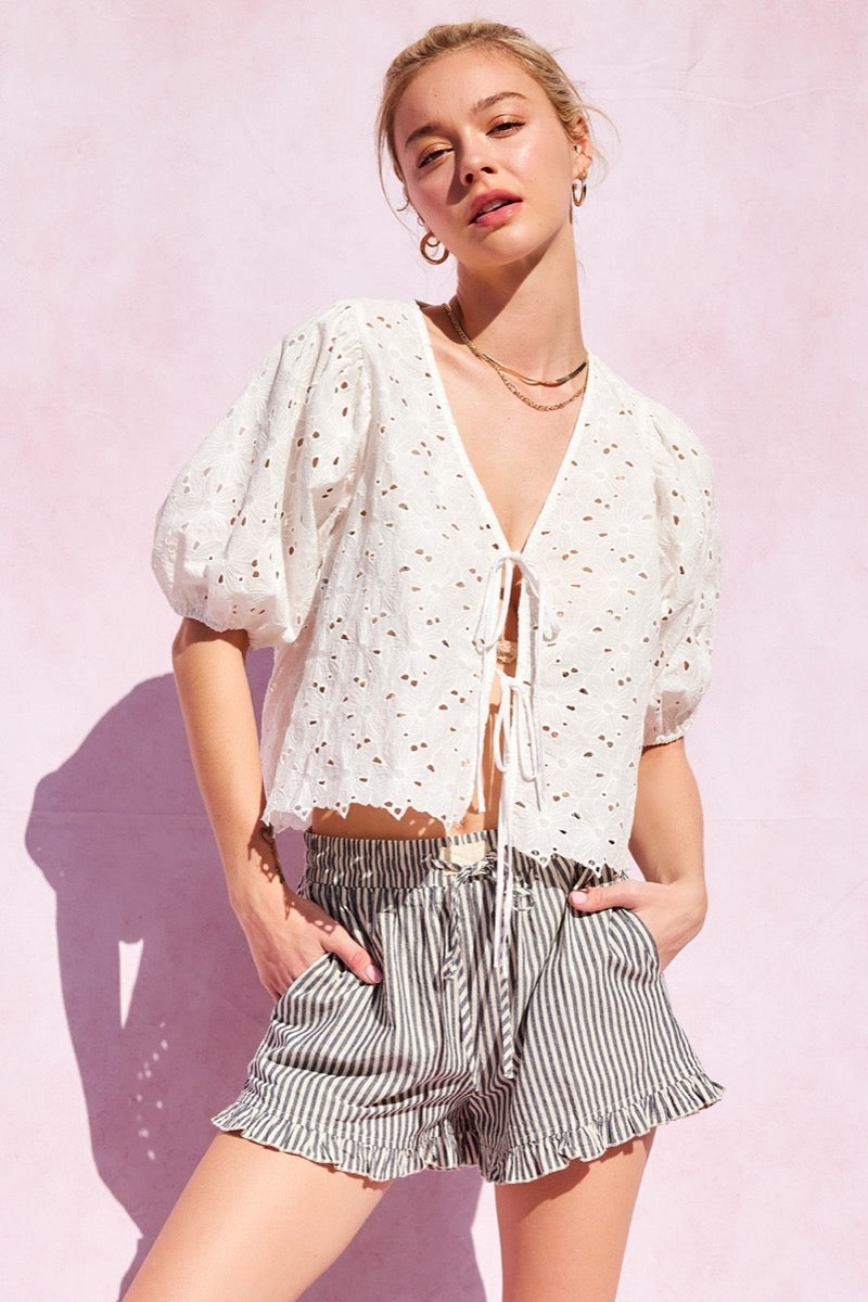 Woman wearing a white blouse with puff sleeves and striped shorts on a pink background