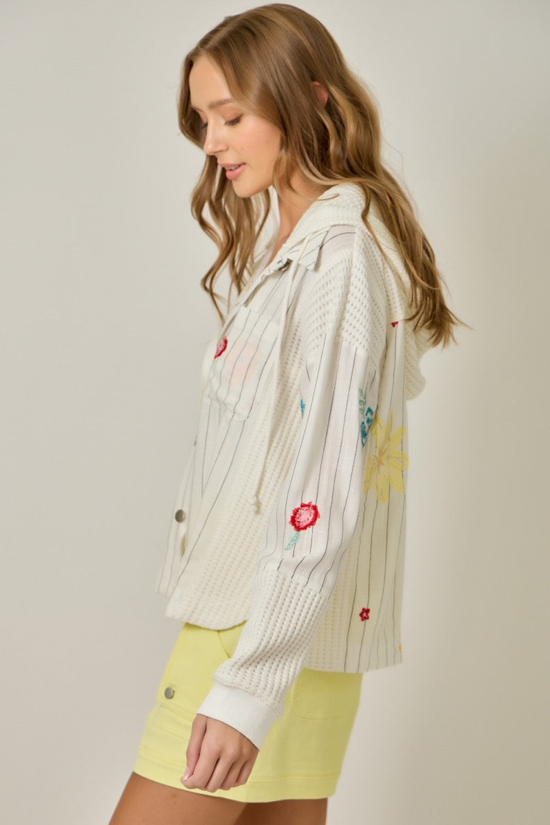 Woman wearing a white embroidered jacket over yellow shorts on a plain background