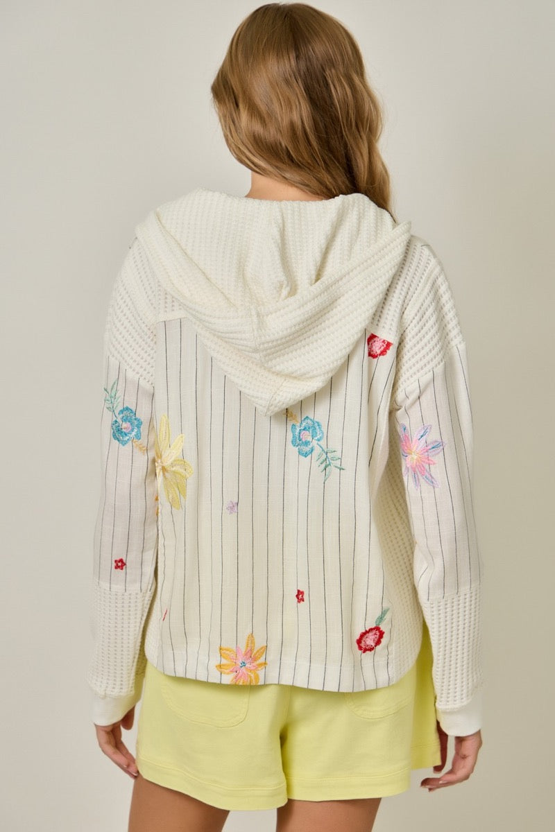 Woman wearing a white jacket with colorful floral embroidery on a plain background